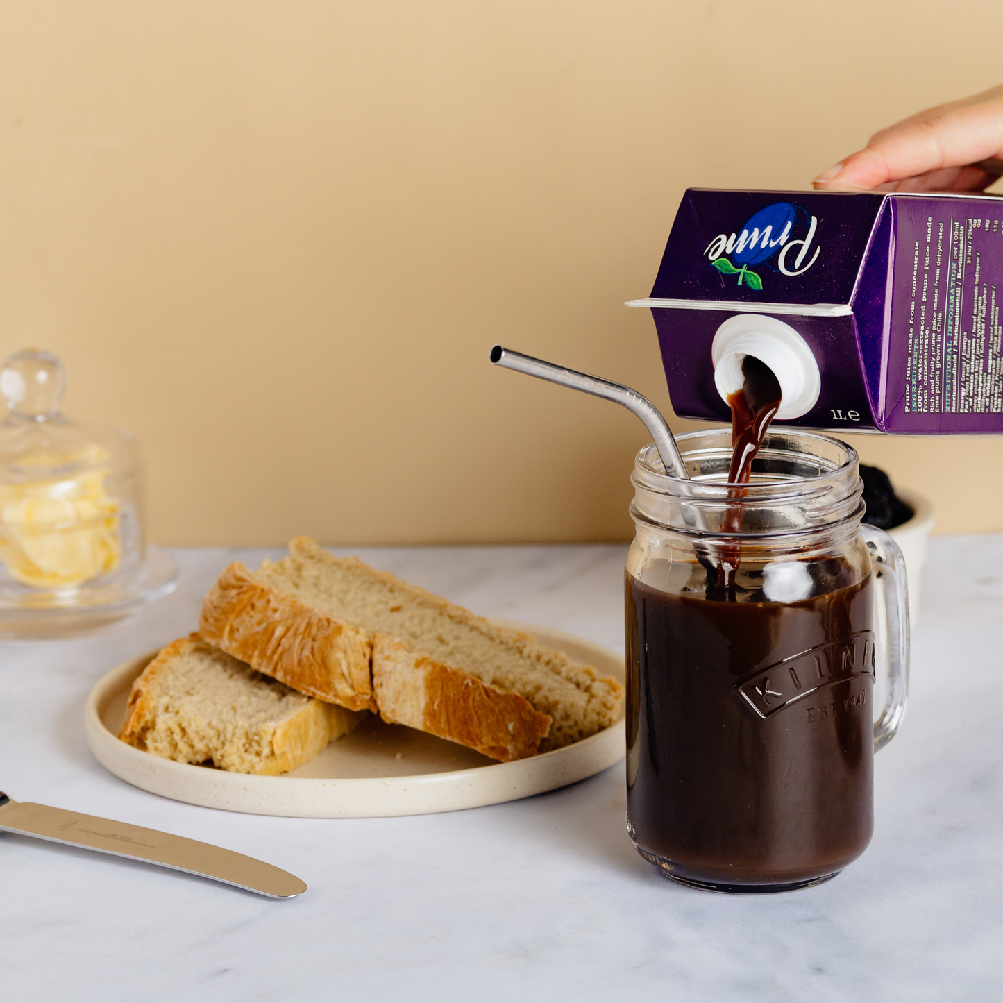 Pouring a carton of prune juice into a glass with toast in the background